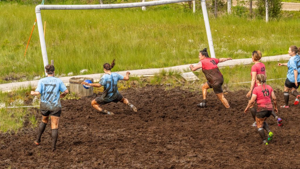 Kaksi naisista koostuvaa joukkuetta pelaavat jalkapalloa suolla. Kyseessä on Suopotkupallon MM-kisat 2025