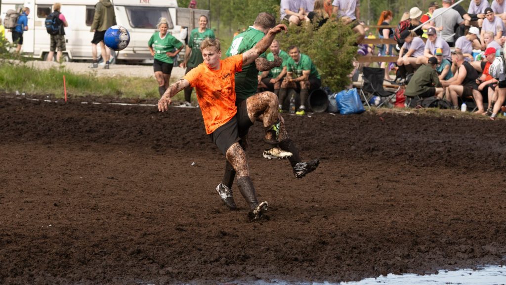 Kaksi miestä pelaavat jalkapalloa suolla. Taustalla yleisöä. Kyseessä on Suopotkupallon MM-kisat 2025