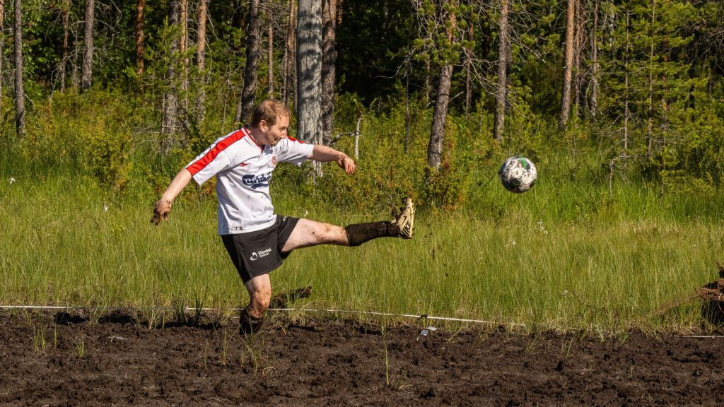 Mies potkaisee jalkapalloa suolla. Kyseessä on Suopotkupallon MM-kilpailut vuonna 2025