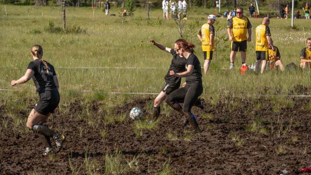 Kolme naista pelaavat suolla jalkapalloa. Kyseessä on Suopotkupallon MM-kilpailut vuonna 2025