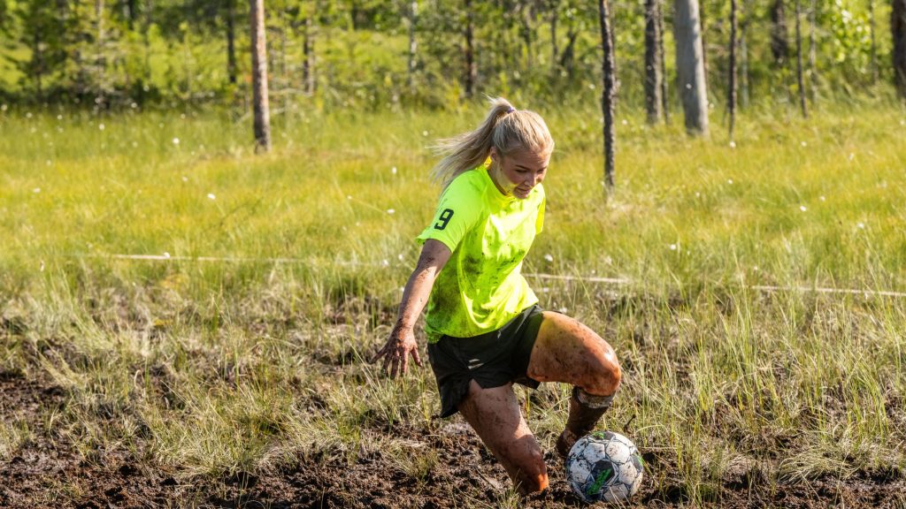 Nainen pelaa jalkapalloa suolla. Kyseessä on Suopotkupallon MM-kilpailut vuonna 2025