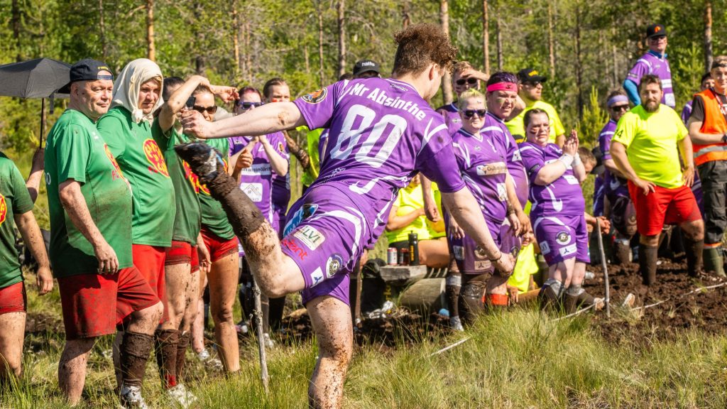 Mies potkaisee jalkapalloa suolla. Taustalla paljon yleisöä. Kyseessä on Suopotkupallon MM-kilpailut vuonna 2025