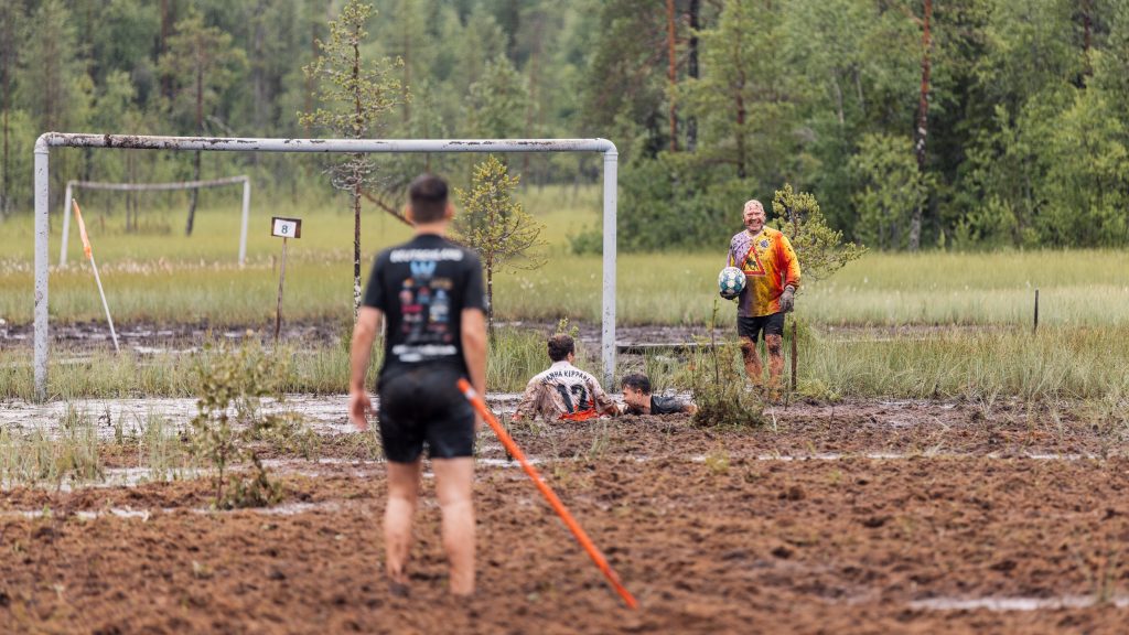 Suomalainen ja saksalainen joukkue pelaavat toisiaan vastaan jalkapalloa suolla. Kyseessä on Suopotkupallon MM-kisat 2024 (In english: Finnish Swamp Soccer team is playing against German team. It is Swamp Soccer World chanpionships 2024)