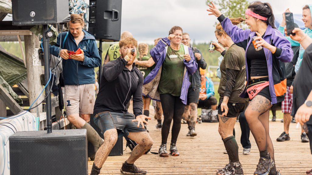 Mies laulaa karaokea suolla ja ymoärillä ihmiset tanssivat. Suopotkupallon MM-kisoissa 2024