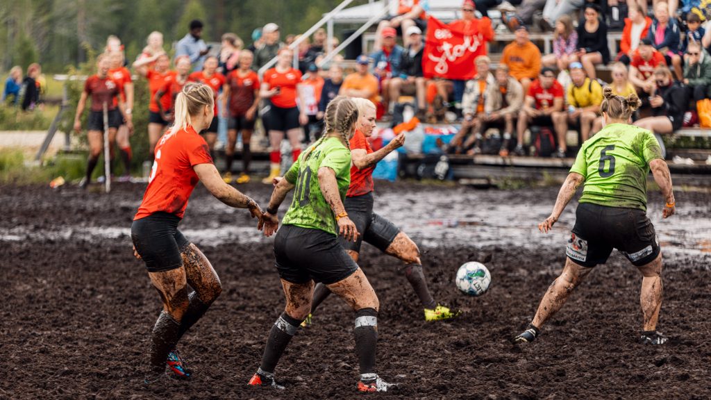 Naiset pelaavat jalkapalloa suolla. Taustalla on yleisöä. Kyseessä on Suopotkupallon mm-kisat 2024