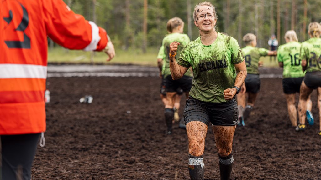 Nainen hymyilee leveästi ja tuulettaa suolla. Kyseessä on suopotkupallon MM-kisat 2024