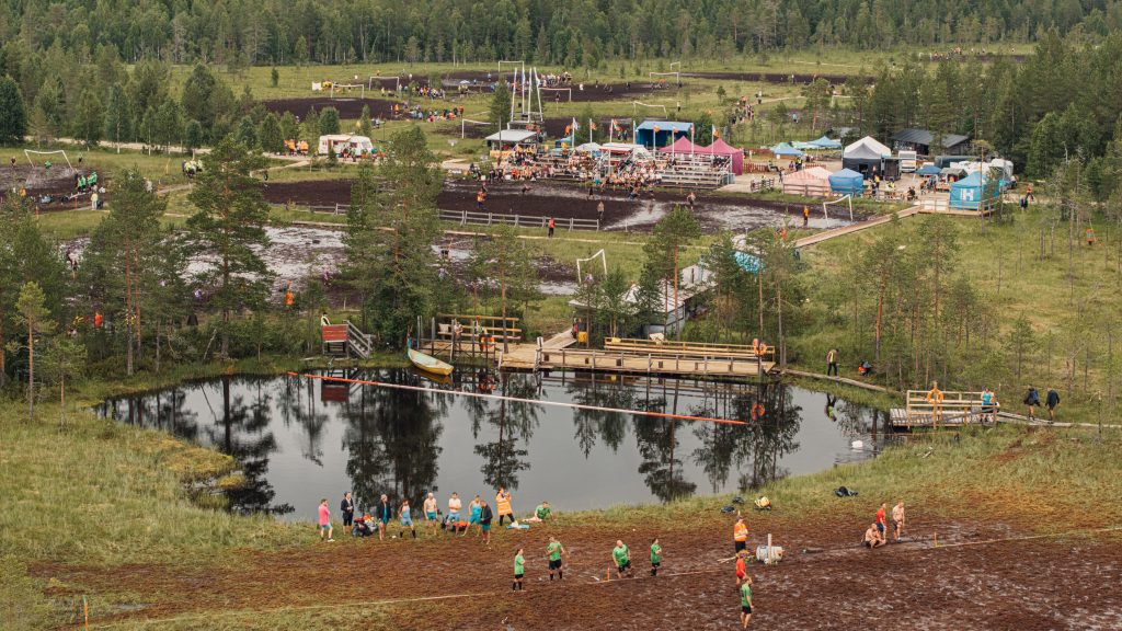 Ilmasta otettu kuva, jossa näkyy suopotkupallo kenttiä, lampi, saunoja, markkinakojuja ja pelaajia. Kyseessä on suopotkupallon MM-kisat 2024